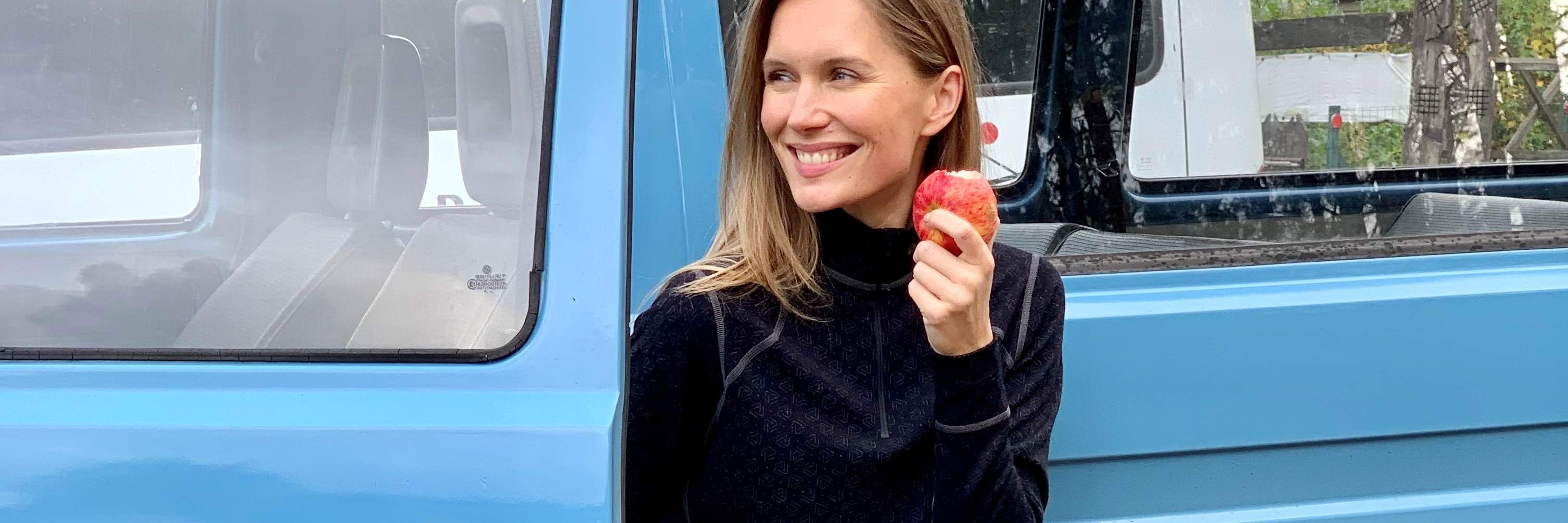 A woman is standing next to an old car and eating an apple