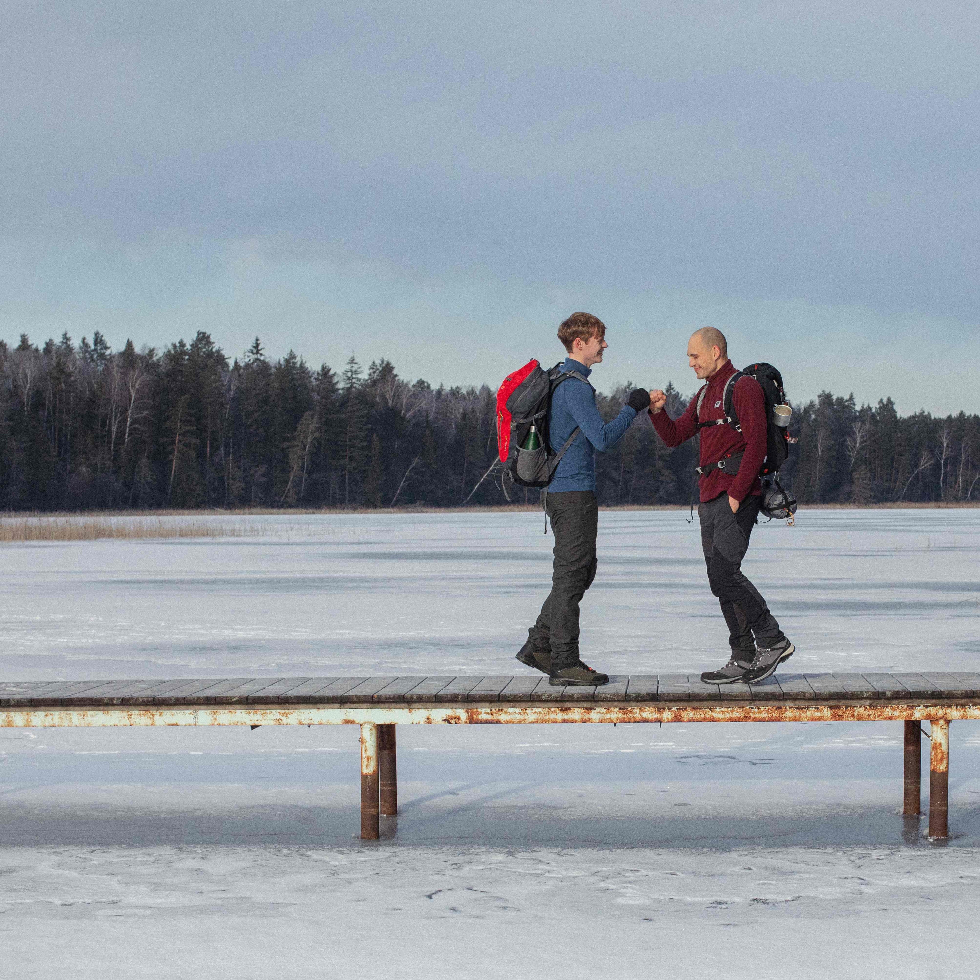 two-men-shakes-hands-on-the-bridge-above-frozen-lake-in-winter
