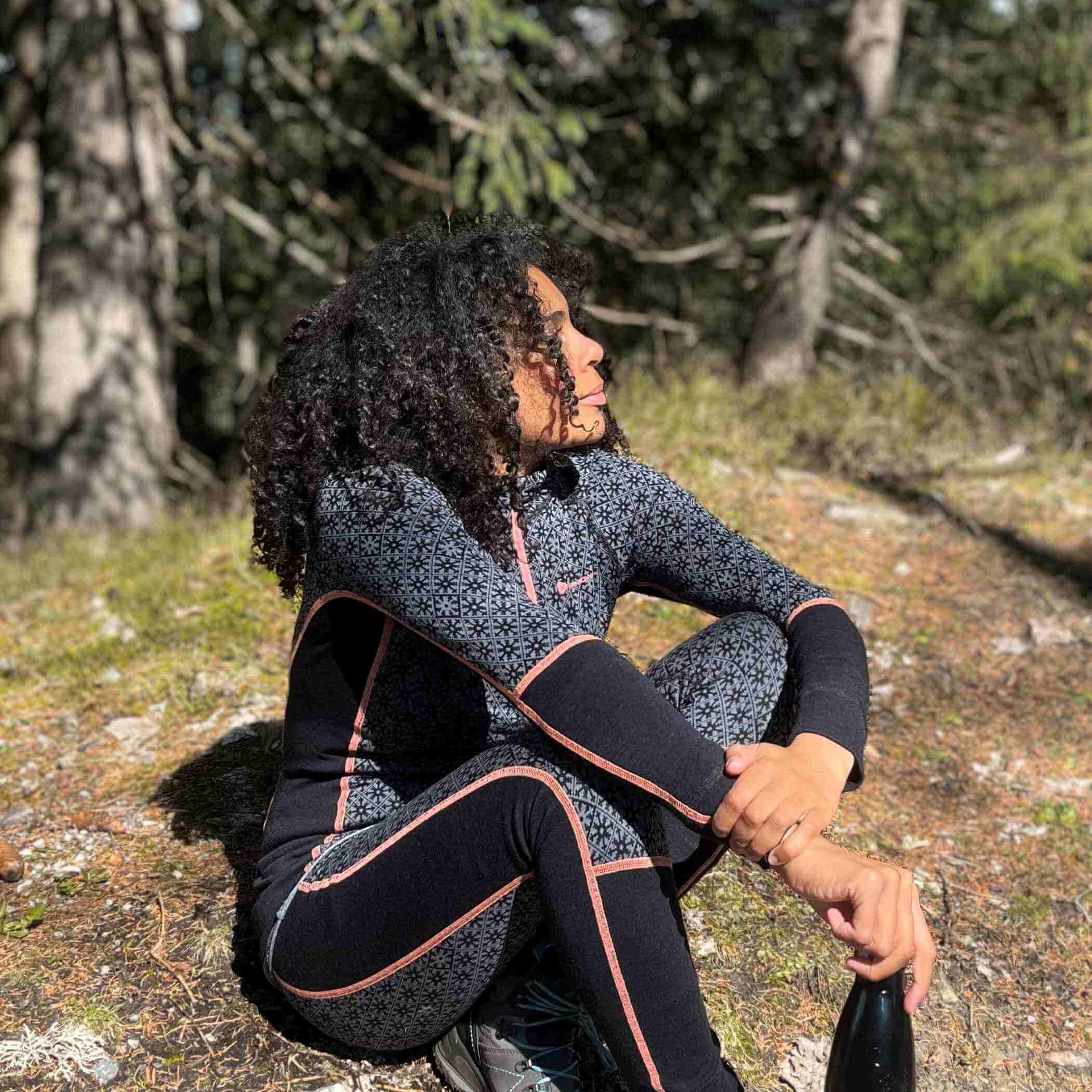 A woman is sitting on the ground in the nature. She is wearing stylish black thermo-clothes