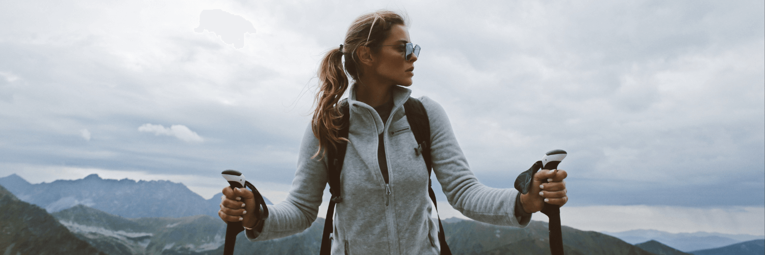 A woman is hiking in the mountains and wearing a lifetime warranty jumper.