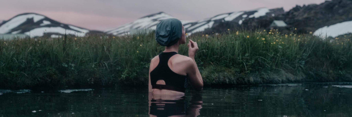 A woman is in the water in cold weather. In the background are mountains