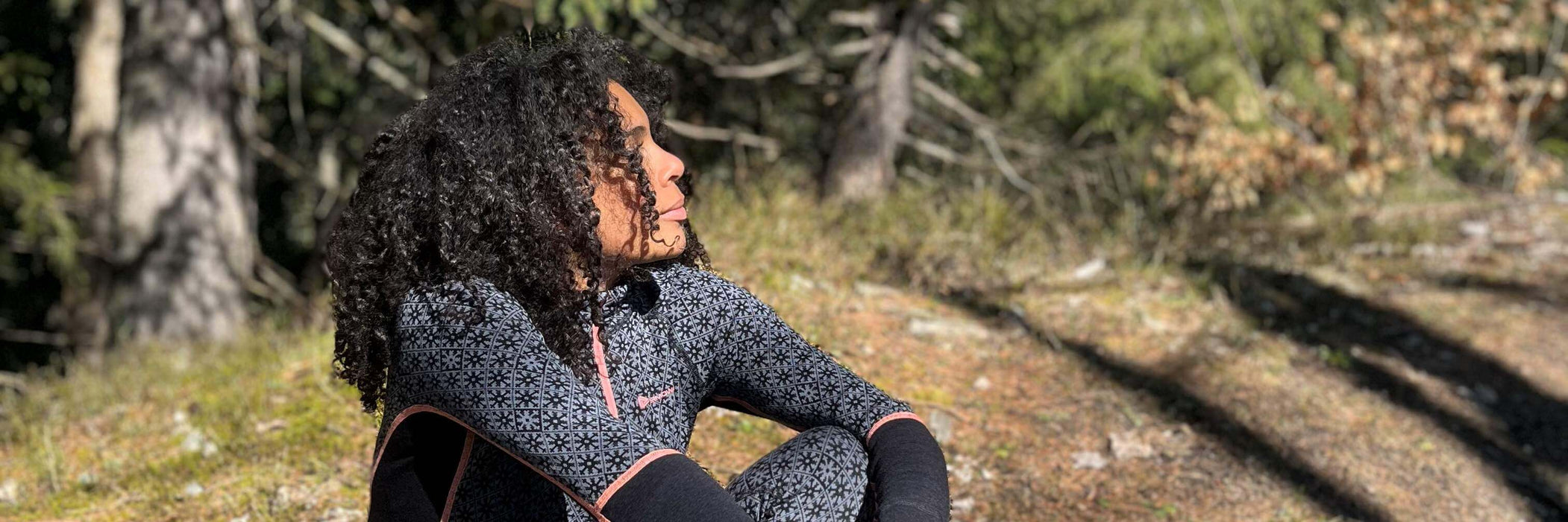 A woman is sitting on the ground in the nature. She is wearing stylish black thermo-clothes
