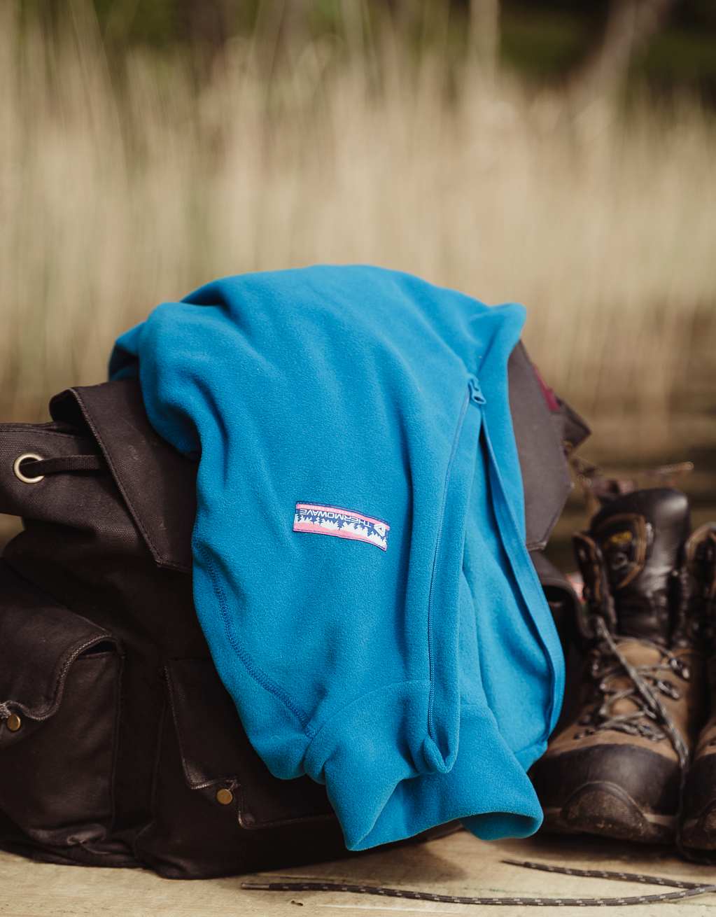 Blue fleece is put on the backpack next to hiking shoes and water