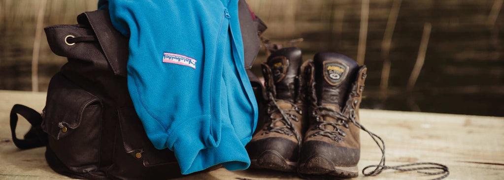 Blue fleece is put on the backpack next to hiking shoes and water