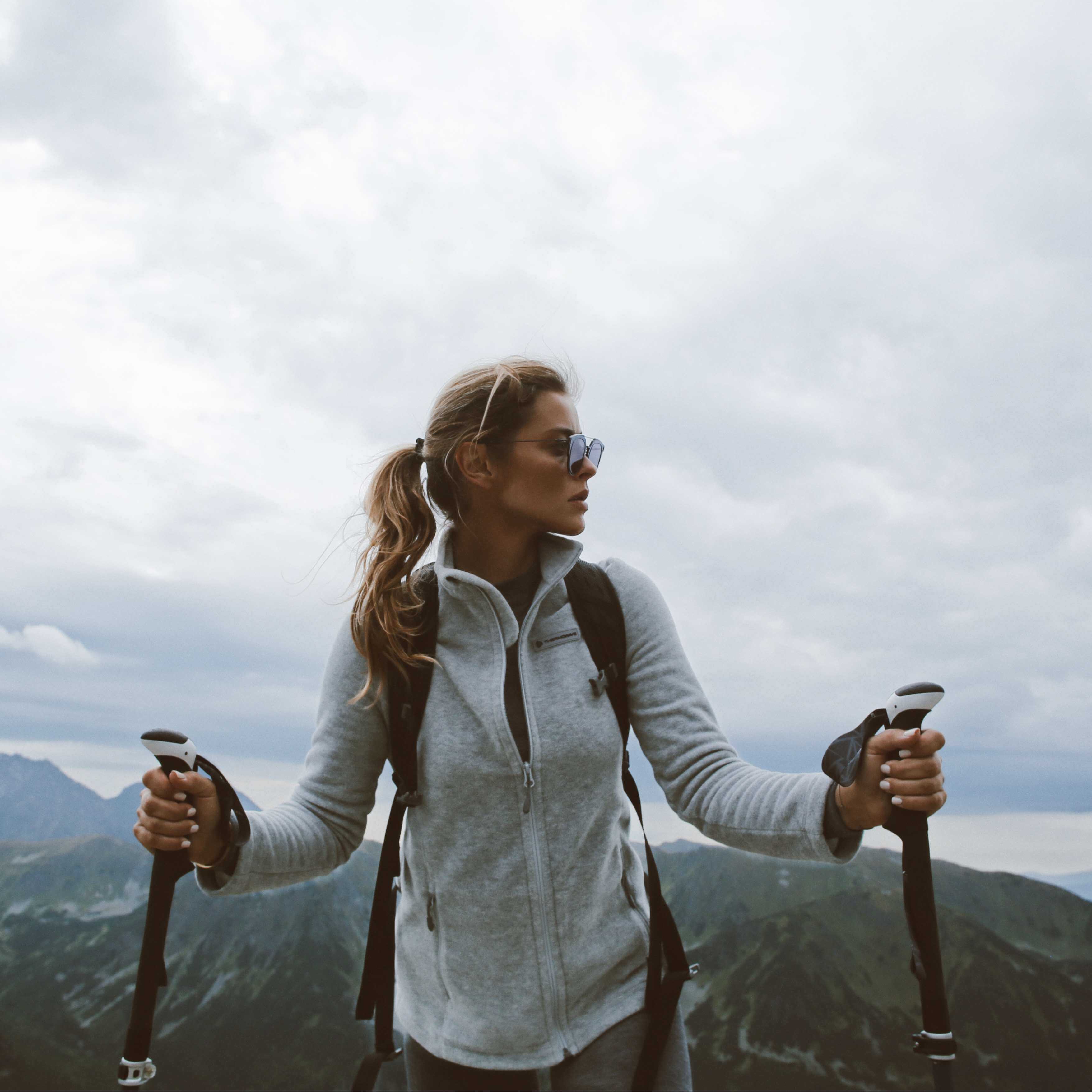 A woman is hiking in the mountains and wearing a lifetime warranty jumper.